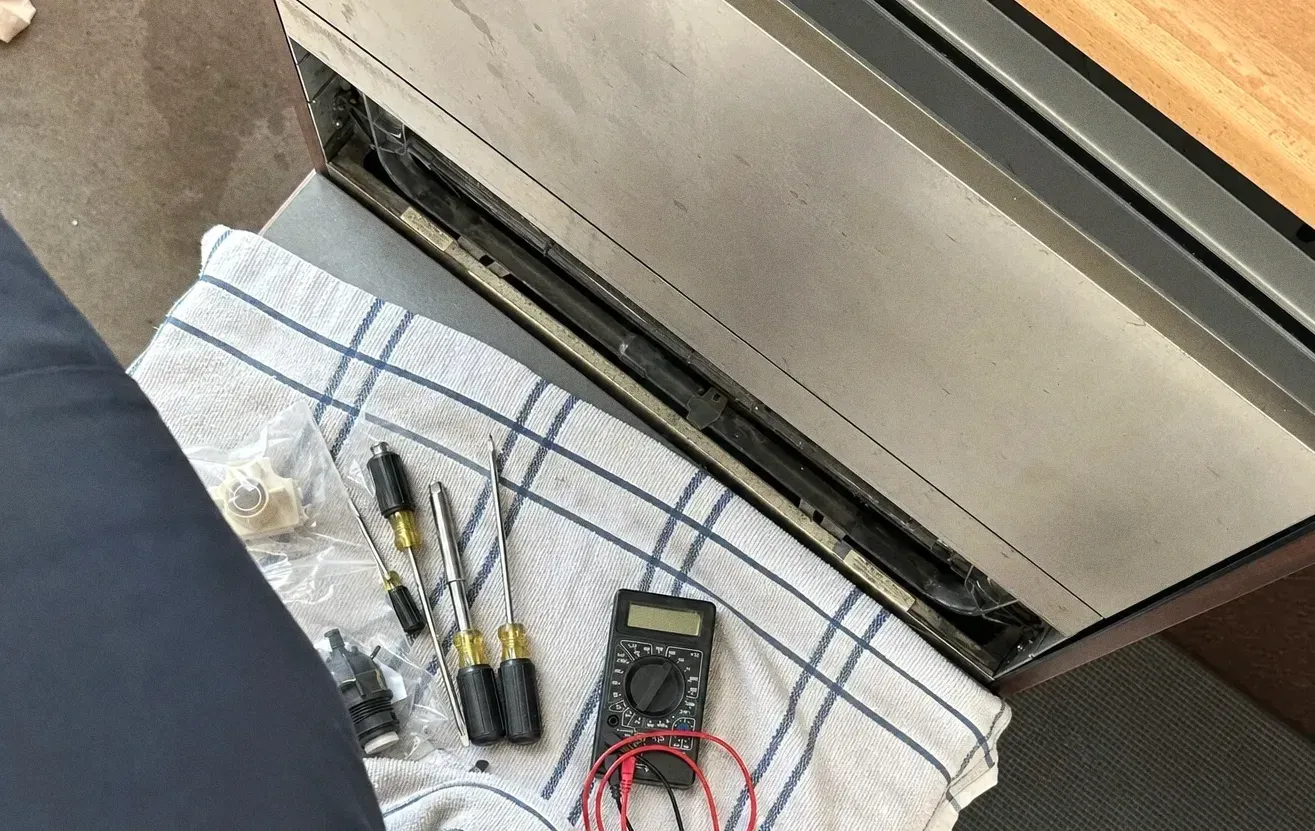 Screwdrivers, a multimeter and small cylindrical components laid out on a folded towel below a stainless appliance base